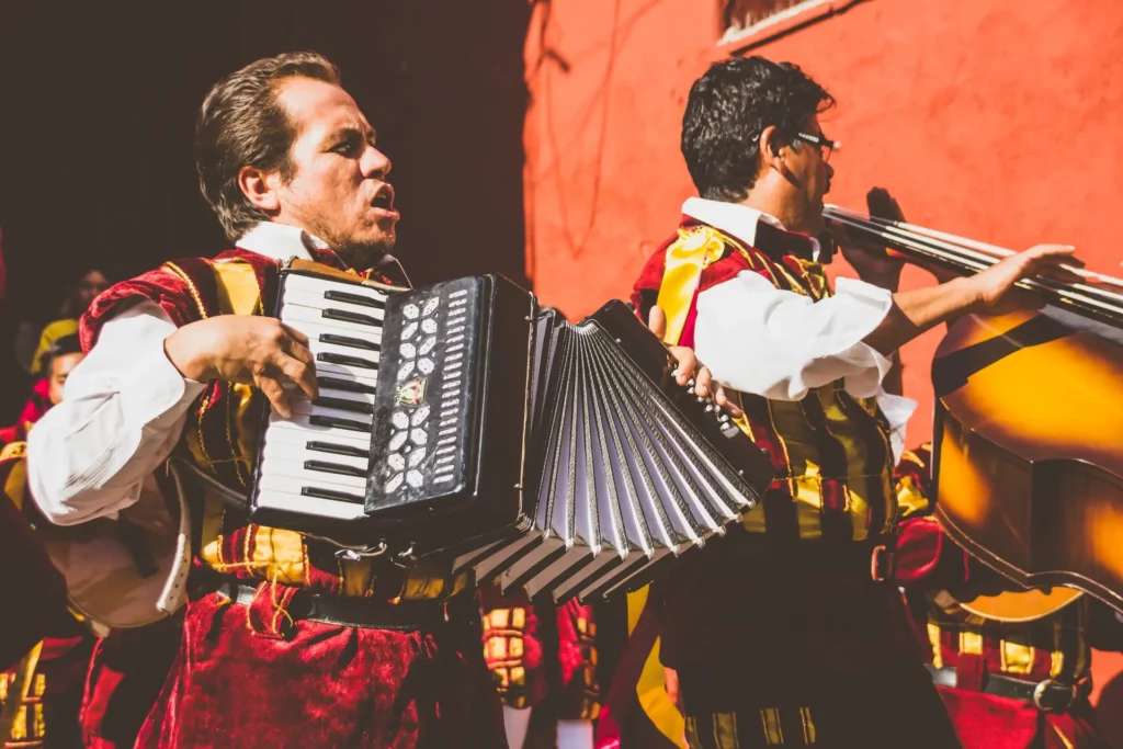 Dois instrumentistas homens, um sanfona e outro com violoncelo tocando durante o dia no México. Reprodução Unsplash.