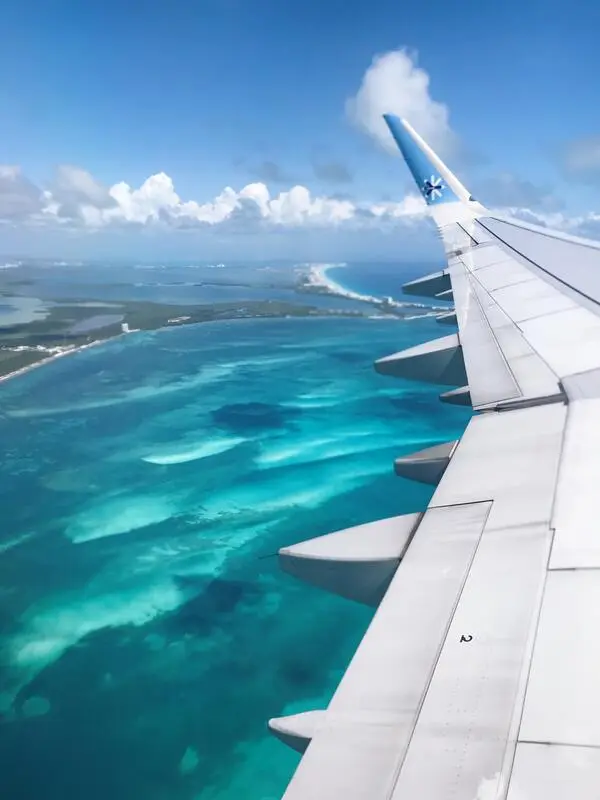 Asa de avião voando sobre praia em Cancún