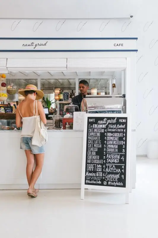 Quanto custa comer em Miami - Mulher de frente para o balcaão de um restaurante conversa como atendente, do lado esquerdo uma lousa com o cardápio e preços